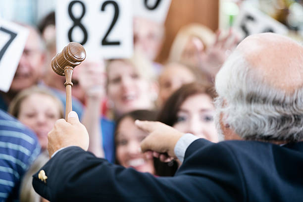 A crowd of bidders at an auction. The focus is on the auctioneer's gavel as he calls out bids.
